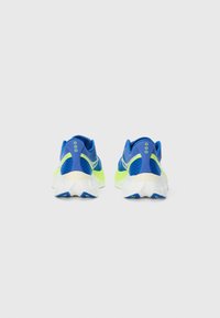 Un par de zapatillas de correr azules y verde neón vistas desde atrás sobre un fondo blanco liso.
