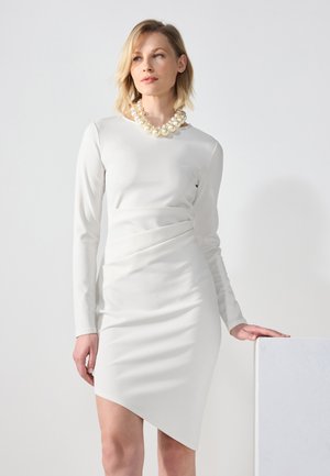 Weißes Langarmkleid mit figurnaher Passform und asymmetrischem Saum. Glatte Textur, mit Raffung am Taillenbereich, kombiniert mit einer auffälligen Perlenkette.