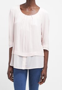 Blusa rosa chiaro con maniche a tre quarti, design a strati, con scollatura rotonda e pieghe sottili sul davanti. Tessuto dalla trama liscia.