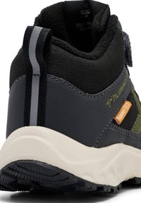 Achterkant van een zwart en donkergrijze sneaker met een witte zool, reflecterende hielband en groene en oranje Hummel Tex branding.