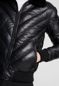 Zwarte leren bomberjack met chevronsteek, ritssluiting aan de voorkant, zijzakken en ribgebreide manchetten en zoom. Zachte afwerking.