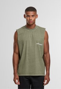 Modello maschile che indossa una maglietta senza maniche di colore verde oliva con la scritta "Sunday Running Club" sul petto, in piedi davanti a uno sfondo grigio chiaro uniforme.