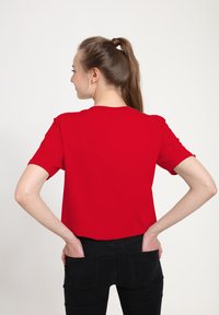 Rød kortærmet t-shirt med rund halsudskæring, lavet af glat stof, parret med sorte jeans med baglommer.