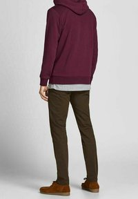 Sudadera con capucha granate con acabado texturizado, camiseta gris debajo, combinada con pantalones ajustados de color verde oscuro y zapatos de ante marrón.