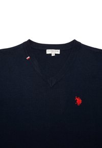 Marinblå v-halsad tröja i stickad tyg, med en liten röd logotyp på vänster bröst och en triangulär sömdetalj vid halsringningen.