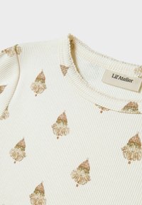 Babytop i mjukt, krämfärgat ribbat tyg med ett återkommande mönster av tecknade tomtar som bär röda hattar. Etiketten säger "Lil'Atelier."