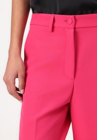 Helderroze, op maat gemaakte broek met een vlakke voorkant, zijzakken en een knoopsluiting bij de taille. Soepele, lichte stof.