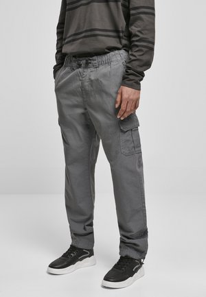 Pantalones cargo grises con una cinturilla elástica, bolsillos laterales y un acabado texturizado. Combinados con zapatillas negras que tienen una suela blanca.