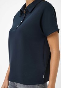 Polo shirt blu navy realizzato in tessuto liscio, con colletto a tre bottoni, maniche corte e una vestibilità morbida. Fessure laterali sottili all'orlo.
