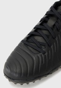 Black soccer shoe featuring a textured synthetic upper, raised ridges, and black laces. Outsole is designed for traction on various surfaces.