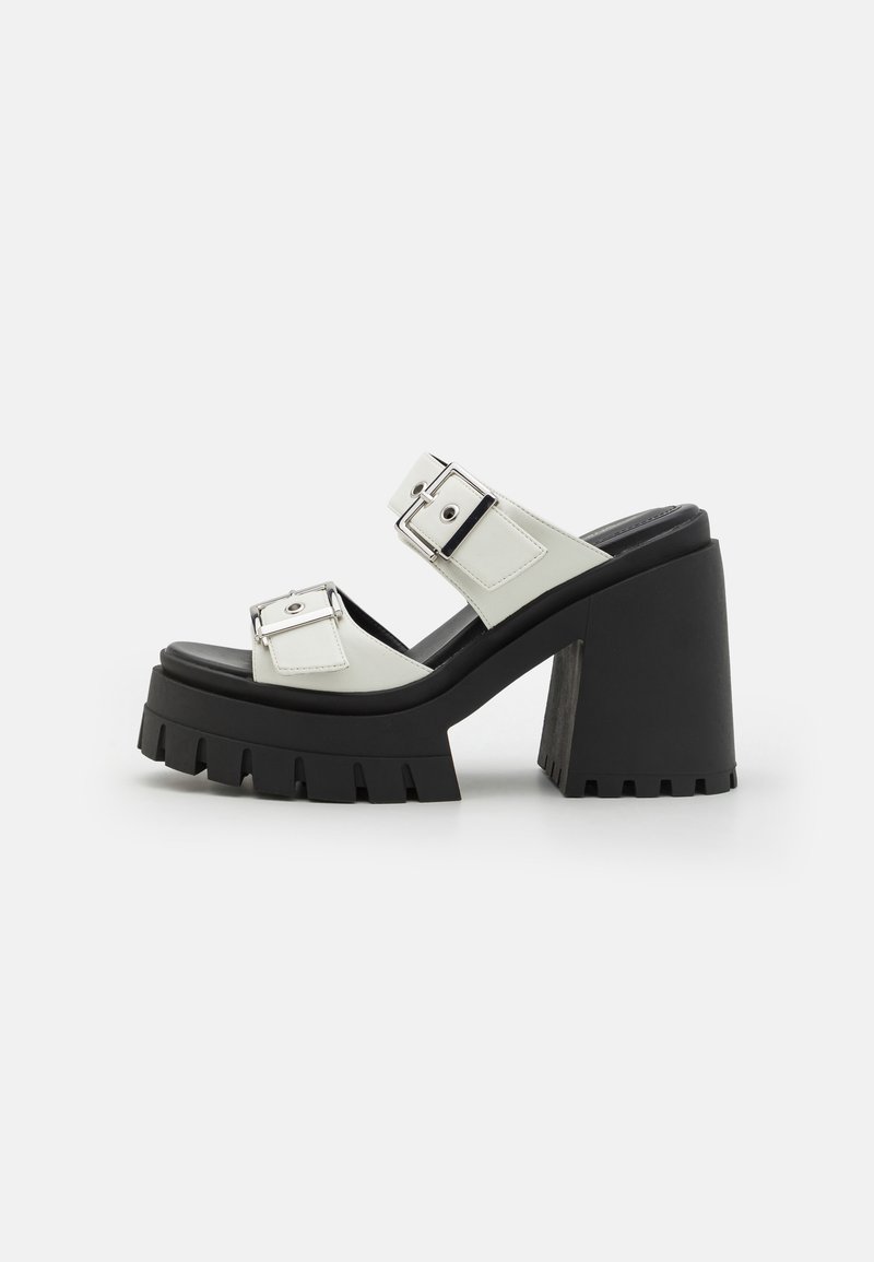 Chunky heel sandal featuring a black rubber sole, white synthetic upper, two adjustable silver buckle straps, and a thick platform base.
