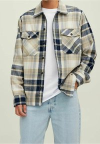 Chemise à carreaux beige et bleu marine avec des boutons sur le devant, deux poches poitrine et un col, assortie à un jean bleu clair.