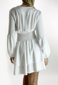 Witte mini-jurk met een smocktail, lange ballonmouwen en een gelaagde rok. Gemaakt van een zachte stof met een vloeiende, relaxte pasvorm.