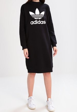 Black sweatshirt dress with long sleeves, white Adidas logo and trefoil design on chest, made of soft fabric, paired with white sneakers.