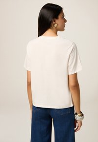 Camiseta de algodón blanca de manga corta y un ajuste ligeramente holgado, combinada con jeans de pierna ancha en azul oscuro. Diseño simple, sin patrones visibles.