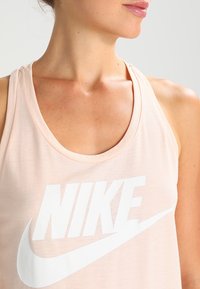 Ljusrosa linne i mjukt tyg med en stor vit Nike-logotyp över bröstet och rund halsringning.