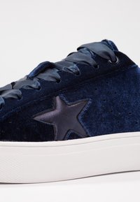 Baskets en velours bleu marine avec lacets en satin, patch en forme d'étoile sur le côté, petits trous de ventilation, et semelle épaisse en caoutchouc blanc.