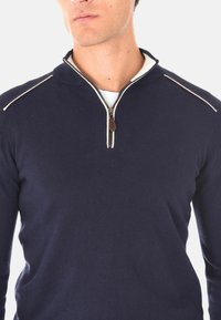 Maglione zip-up blu navy realizzato in morbido tessuto, con colletto alto e dettagli a punto crema sulle spalle. Zip decorativa con un accento marrone.