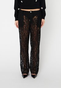 Pantaloni in pizzo nero con un motivo floreale, design a gamba dritta, tessuto trasparente e chiusura con bottone frontale.