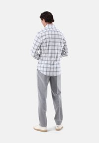 Camicia a scacchi grigia e bianca con colletto button-down, abbinata a pantaloni grigi chiari e scarpe bianche, vista da dietro.