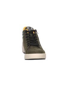 Baskets vert olive avec lacets noirs, tige en cuir, semelle en caoutchouc fine, accents jaunes et patch logo sur la languette.