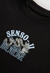 Svart bomullströja med grafisk design som har två drakar och texten "SENSO-II" i ljusblå och vit sömnad.