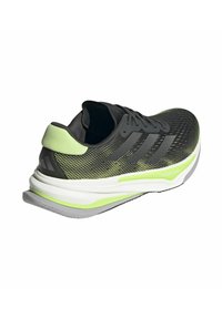 Scarpa da corsa nera con parte superiore in rete, accenti verde brillante, intersuola bianca spessa e suola grigia. Presenta un motivo testurizzato e tre strisce.