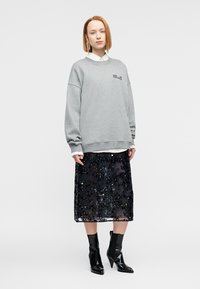 Γκρι φούτερ με χαλαρούς ώμους και λογότυπο, φορεμένο πάνω από μαύρη μίντι φούστα με παγιέτες, συνδυασμένο με μαύρα μποτάκια αστραγάλου.