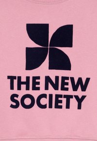Ροζ φούτερ με μεγάλο σχέδιο μαύρου λογότυπου που περιλαμβάνει στρογγυλεμένα σχήματα και το κείμενο "Η ΝΕΑ ΚΟΙΝΩΝΙΑ" σε παχιά μαύρη γραμματοσειρά.