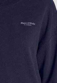 Sudadera de cuello redondo color azul marino, confeccionada en tejido suave, con un estampado de logo blanco "Marc O'Polo" en el pecho y cuello de canalé.