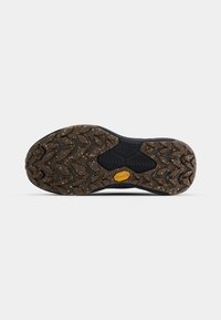 Semelle de chaussure en caoutchouc noire avec un motif texturé en zigzag. Présente un logo Vibram jaune bien en vue et de petites speckles çà et là.