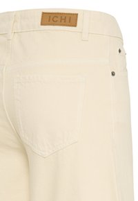 Kremfarvede denimjeans med baglomme og brun lædermærke med mærket "ICHI" på linningen.