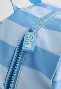 Sac à dos à rayures bleues avec une fermeture éclair et une tirette bleu clair étiquetée "Bluey". Fabriqué en matériau durable, texture lisse et couleurs vives.
