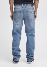 Light blue denim jeans with a relaxed fit, featuring two back pockets and a leather brand patch on the waistband. Worn with black sneakers.