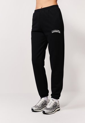 Czarne dresy z elastycznymi mankietami, z kieszeniami bocznymi i haftowanym logo "LAMANIA". W połączeniu z srebrnymi butami sportowymi i białymi skarpetkami.