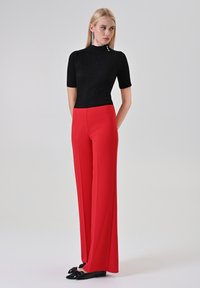 Top nero a maniche corte con coste abbinato a pantaloni rossi a gamba larga e vita alta, evidenziati da un dettaglio con bottoni sul collo e ballerine nere.