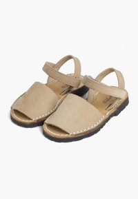 Beige-nahkaiset lasten sandaalit avonaisilla varpailla, säädettävillä nilkkahihnoilla, valkoisella ommella ja mustilla kumipohjilla valkoisella taustalla.