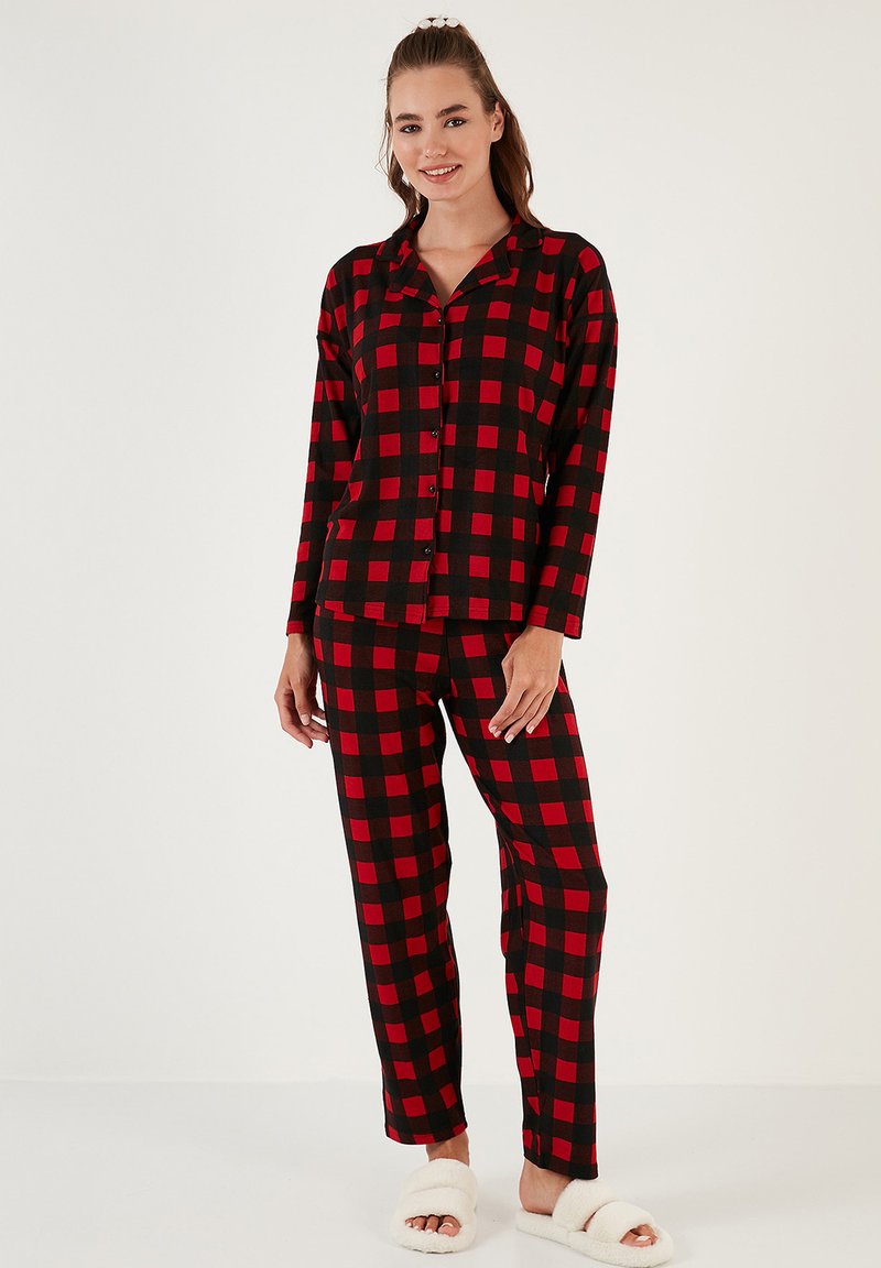 Conjunto de pijama a cuadros rojos y negros con mangas largas y cierre de botones, que incluye pantalones holgados, acompañado de pantuflas blancas y suaves.