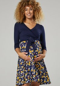 Maternity dress featuring a navy top with three-quarter sleeves and a floral-patterned skirt in navy, yellow, and white. Ties at the waist.