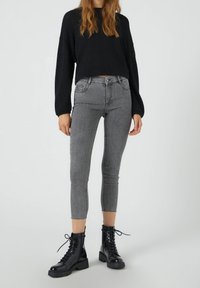 Jeans skinny de talle alto en color gris con dobladillo deshilachado, combinados con un suéter corto negro y botas de combate negras con cordones. Textura de denim suave.