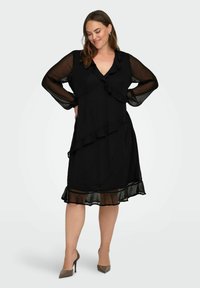 Czarna sukienka z przezroczystymi długimi rękawami, z falbaniastym wykończeniem i warstwowym dołem. Gładka tekstura i kształt A sprawiają, że prezentuje się elegancko.