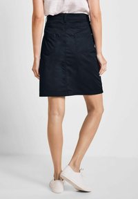 Jupe en denim noir avec une coupe droite, dotée de deux poches à l'arrière et d'une ceinture. Associée à des baskets de couleur claire.