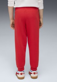 Pantaloni sportivi rossi con vita elastica, vestibilità affusolata e polsini alle caviglie. Indossati con scarpe multicolori con dettaglio del logo.