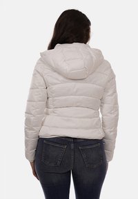 Giacca bianca gonfia con cappuccio, caratterizzata da un motivo a quadrati orizzontali, chiusura con zip e un design aderente, abbinata a jeans in denim scuro.