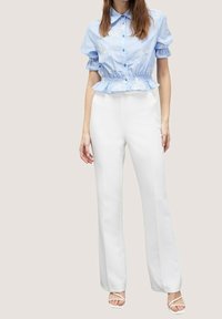 Blue short-sleeve blouse with embroidered accents, fitted waist, and pleated hem paired with white, straight-leg trousers and strappy sandals.