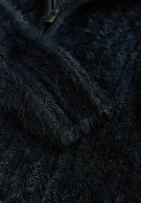 Tissu en fausse fourrure bleu marine foncé avec une surface douce et duveteuse. Présente une fermeture éclair avec un accent en métal, mettant en valeur la texture pelucheuse et la couleur riche.