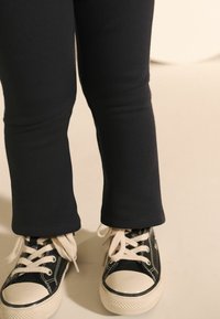 Leggings noires côtelées avec une coupe ajustée, associées à des baskets noires avec des semelles en caoutchouc blanc et des lacets beiges.