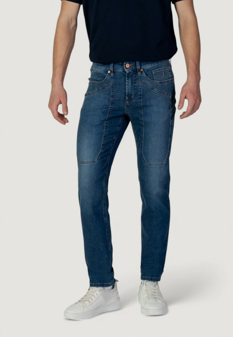 Jeans in denim di un blu scuro con una leggera scoloritura, slim fit, cinque tasche e cuciture a contrasto; indossati con sneaker bianche.
