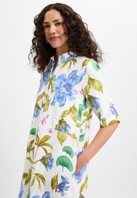 Bloemenhemdjurk van lichtgewicht witte stof met blauwe en groene patronen, een knoopkraag en een borstzak. Korte mouwen.
