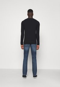 Maglietta nera a maniche lunghe abbinata a jeans di denim blu. La maglietta ha uno scollo rotondo; i jeans sono aderenti con tasche posteriori.